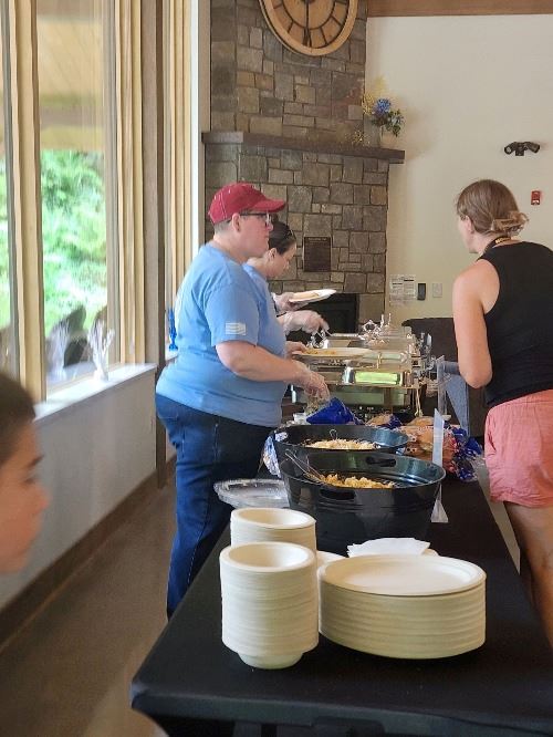 Volunteers serve food to attendees in the serving line at the Veteran Family BBQ.