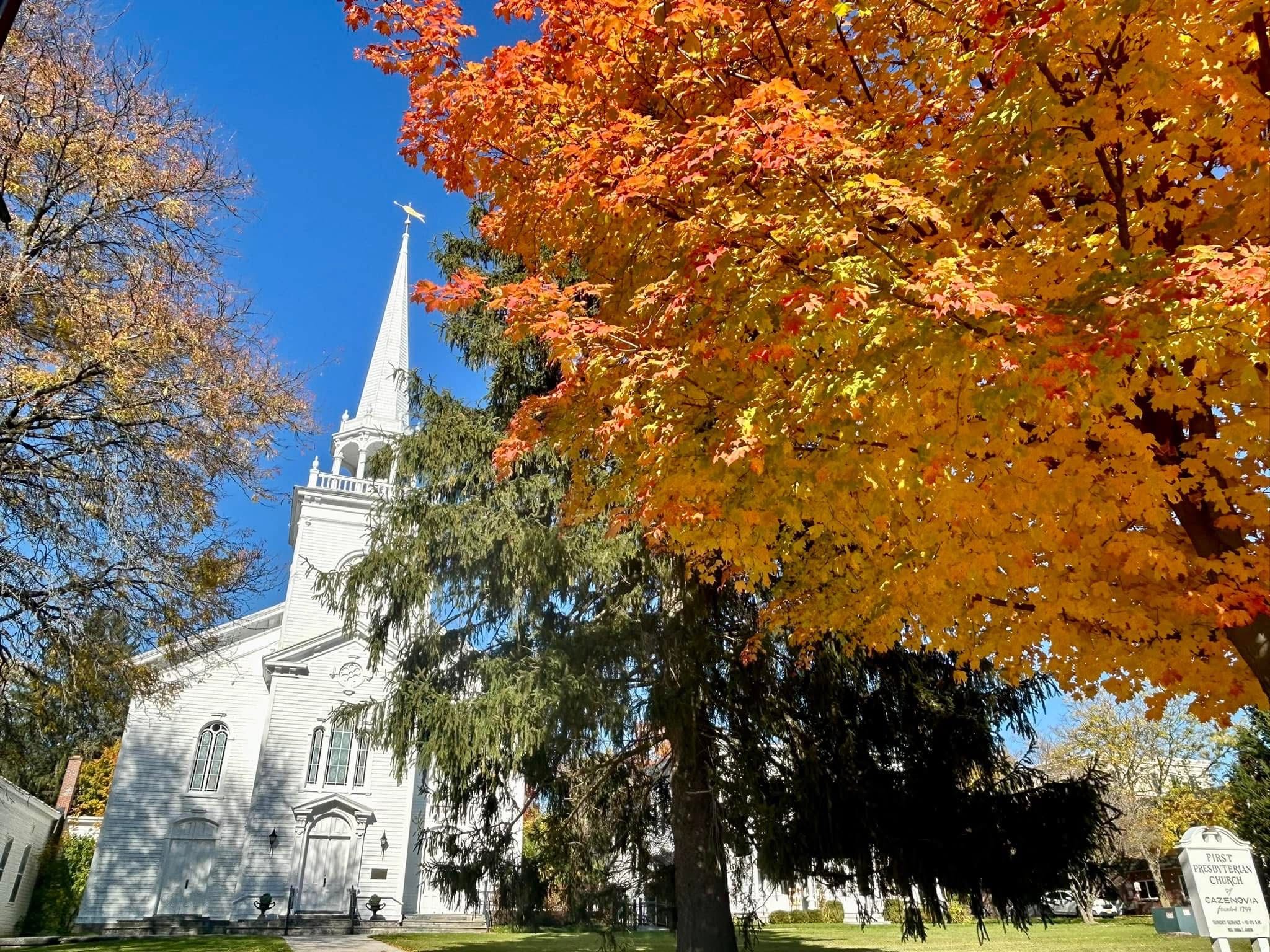 Picture taken by J. Wallace of a white church with an orange fall tree in the foreground. 