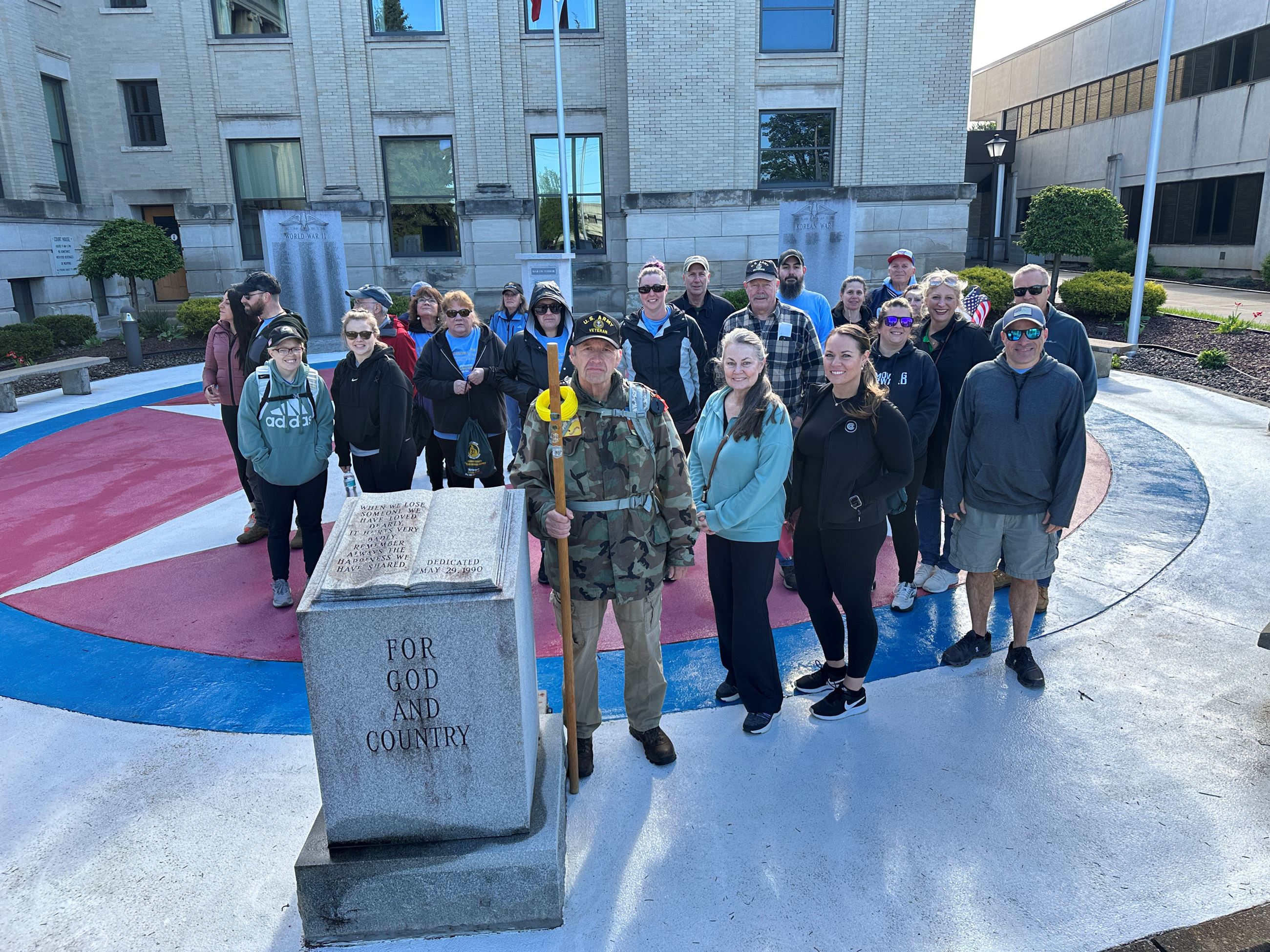 A group of participants pose together near a veterans memorial outside the courthouse during the 2025 Veteran Hike event.